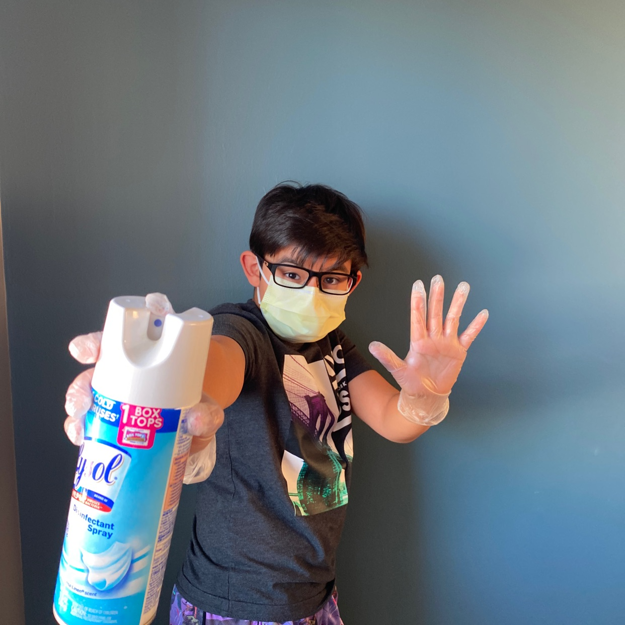 A child wearing a face mask, rubber gloves, and holding a spray bottle of disinfectant