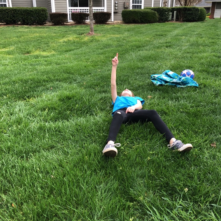 A child lying in a field of grass pointing at the sky