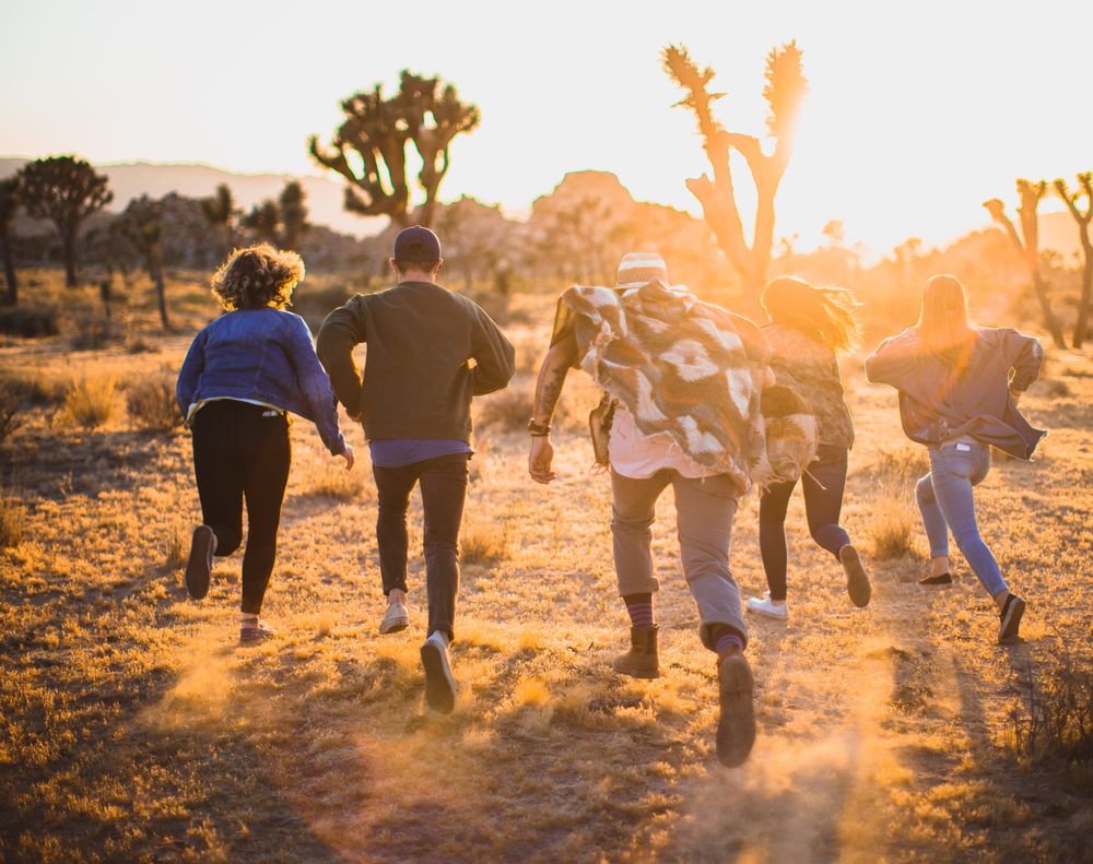 five people running through a desert at sunset